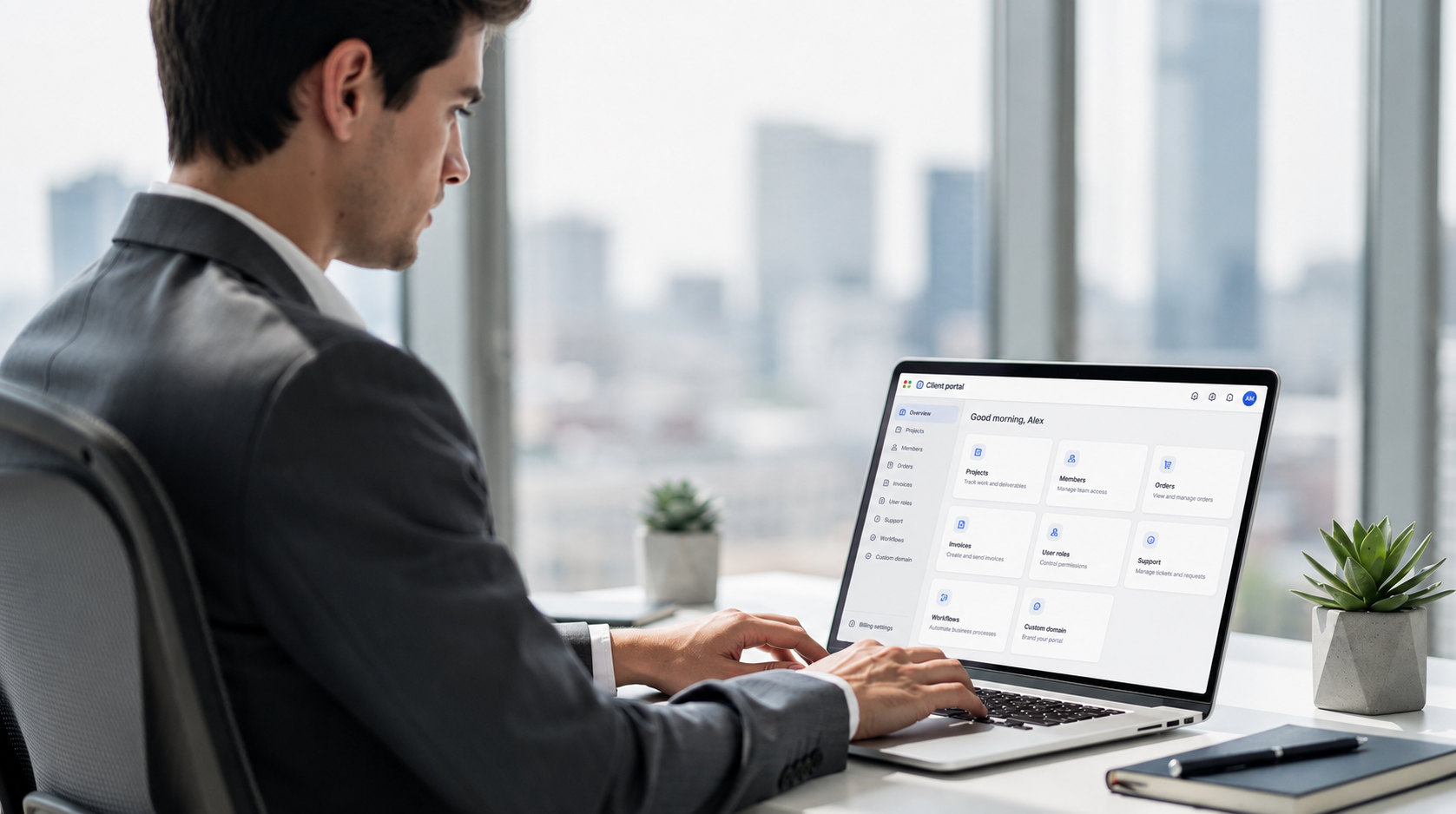 A person is focused on their laptop in a bright, modern office, developing a web application interface that enhances business operations and creates custom portals for client-facing systems. The workspace is equipped with tools for data analysis and project tracking, reflecting a user-friendly environment for managing complex projects.