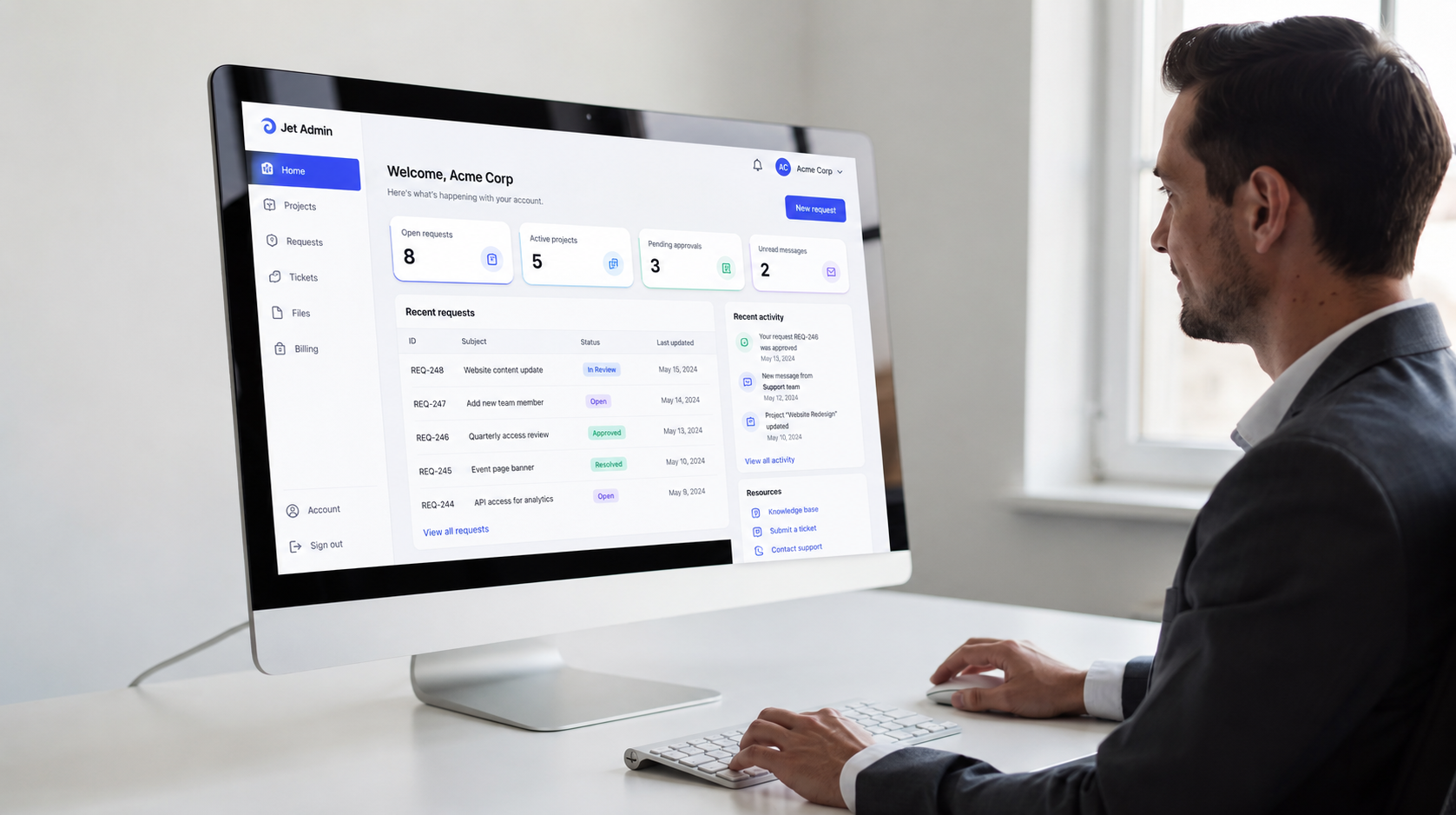 The image shows a professional focused on a branded client portal interface displayed on a large monitor, featuring the company’s colors and a clean sidebar navigation for easy access to project management tools and support requests. The setup emphasizes a user-friendly experience for managing tasks and client communication.