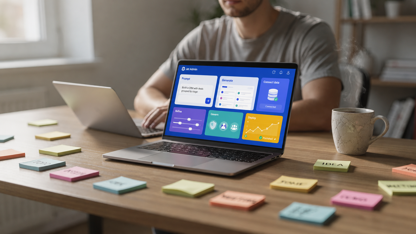 A person sits at a desk using a laptop with a colorful visual interface, showcasing a no code app builder. The workspace is filled with sticky notes and a coffee mug, highlighting a creative environment for building web apps and automating workflows.